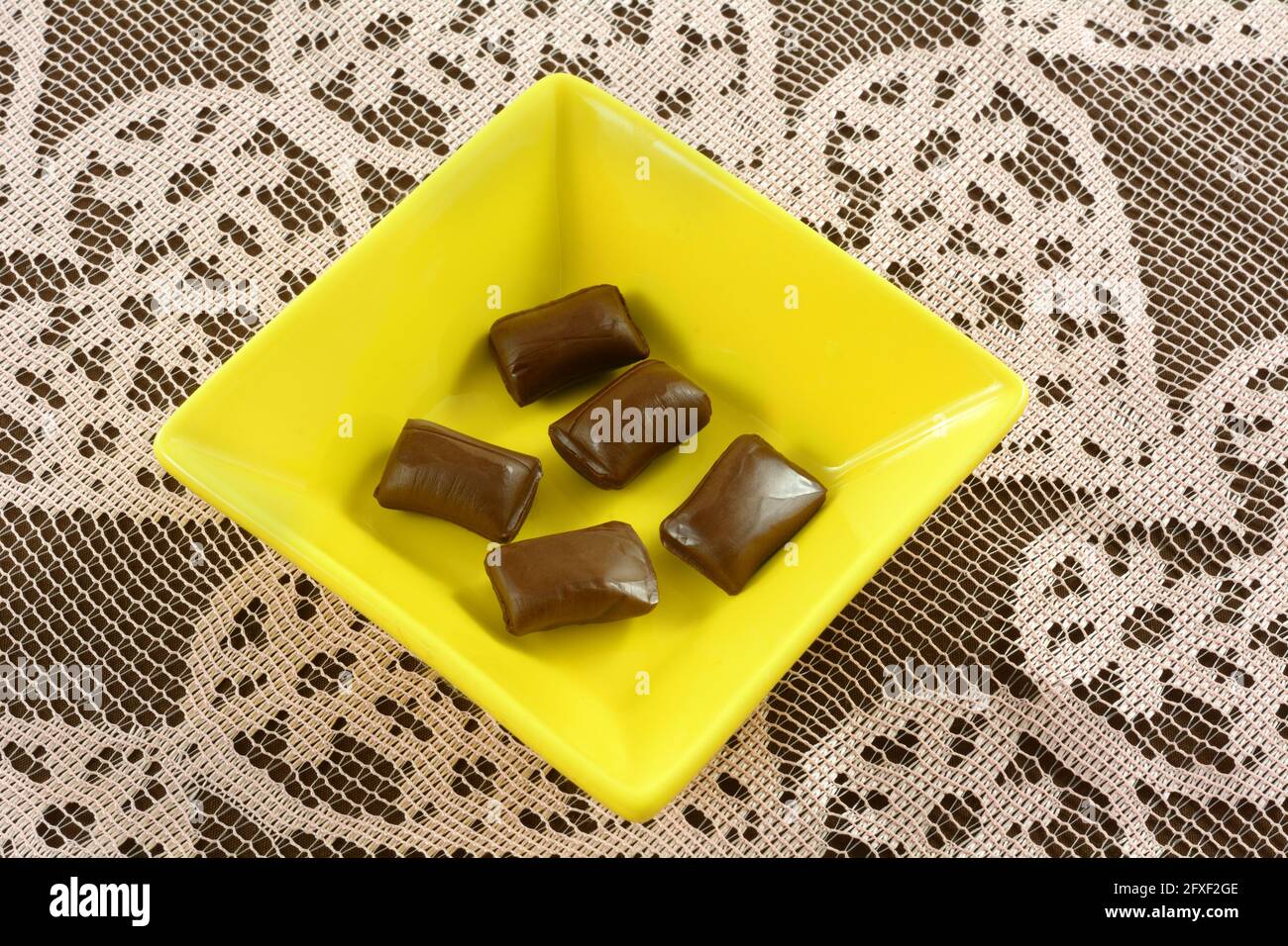 Schokoladen-Süßigkeiten in gelben Bonbons auf Tischdecke aus rosa Spitze mit Herzmuster Stockfoto