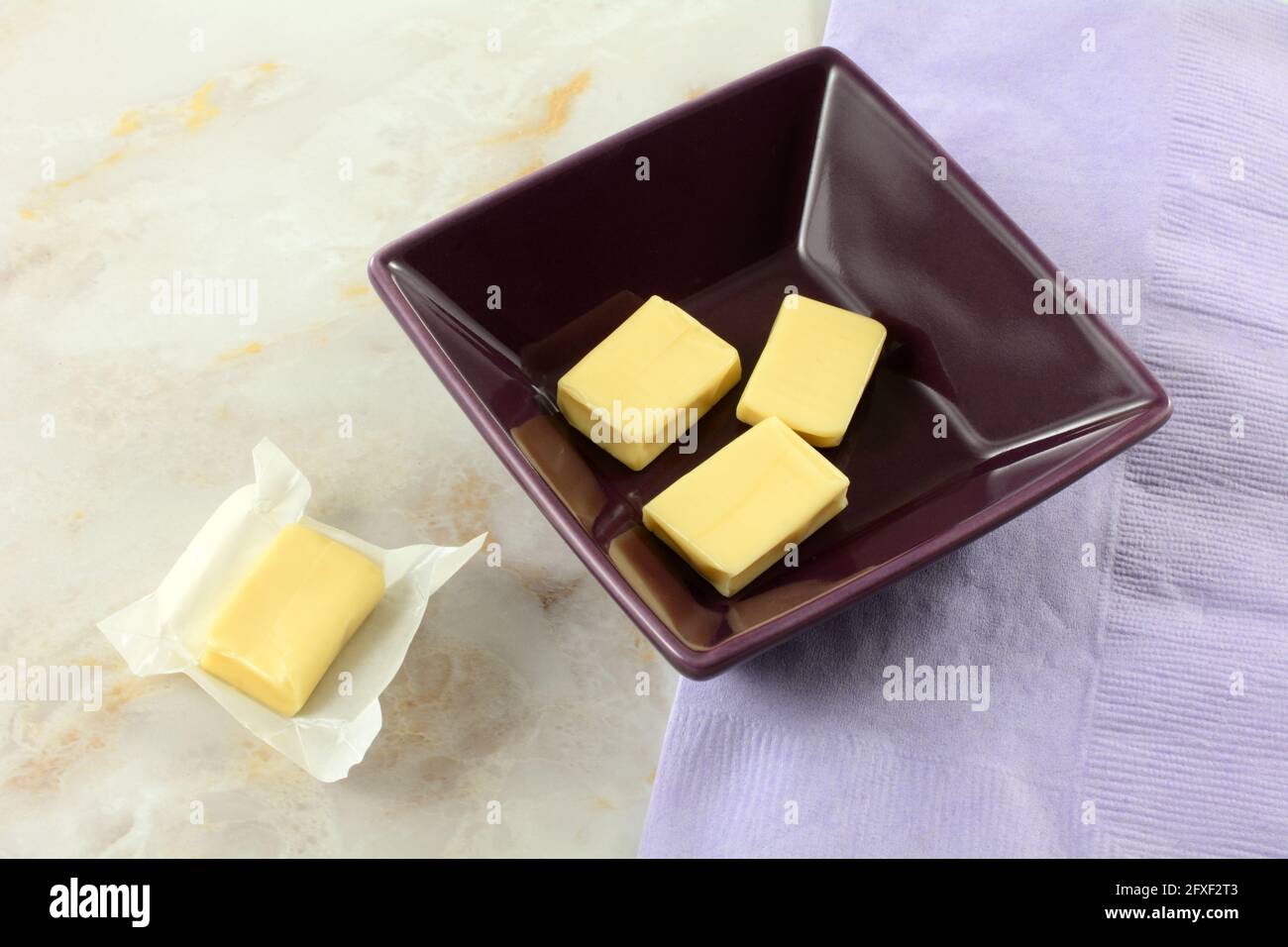 Joghurt, kauen Süßigkeiten in lila Schüssel und eine in Geöffnete Süßigkeitenverpackung mit Lavendelserviette Stockfoto