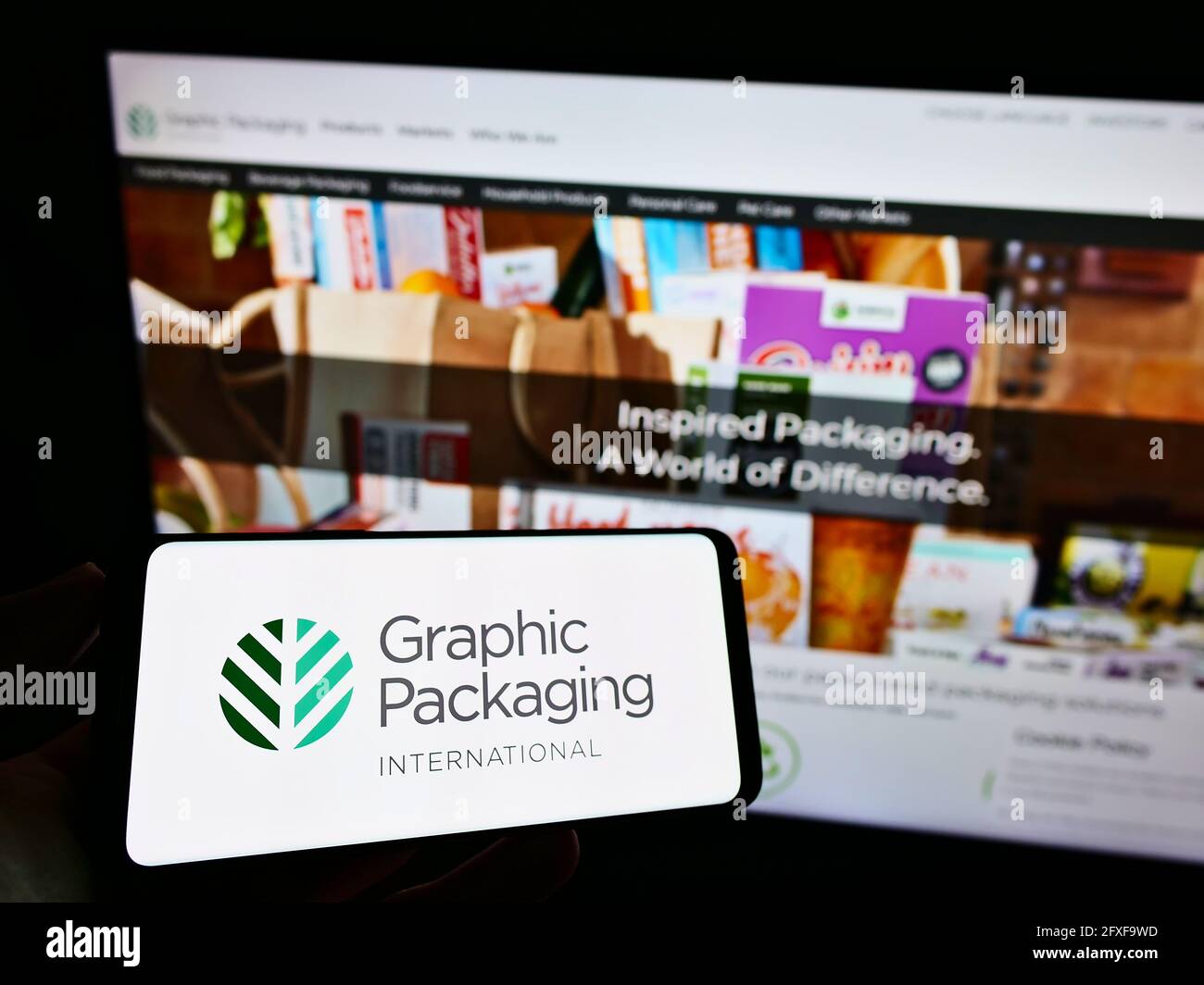 Person, die Mobiltelefon mit dem Logo der amerikanischen Firma Graphic Packaging International LLC auf dem Bildschirm vor der Webseite hält. Konzentrieren Sie sich auf die Telefonanzeige. Stockfoto