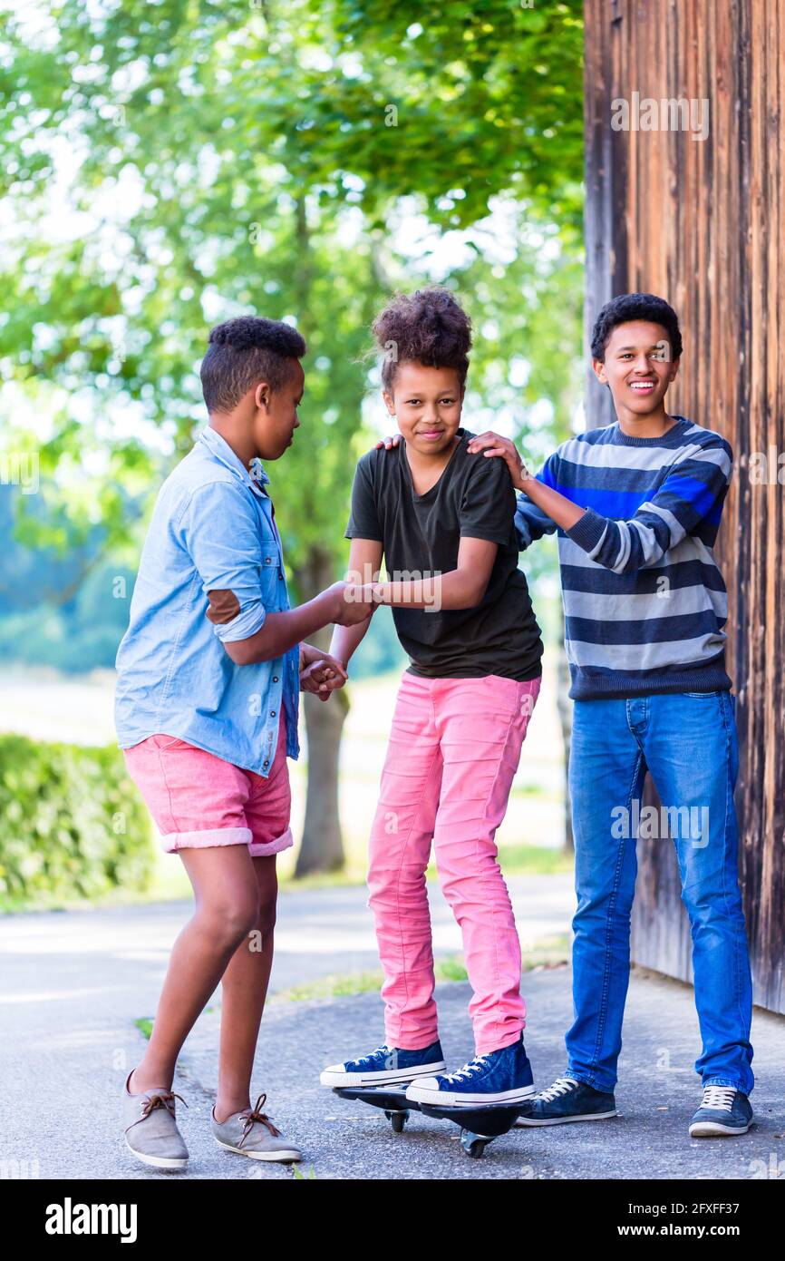 Drei schwarze Kinder, Jungen und Mädchen, Spielen zusammen mit Skateboard Stockfoto