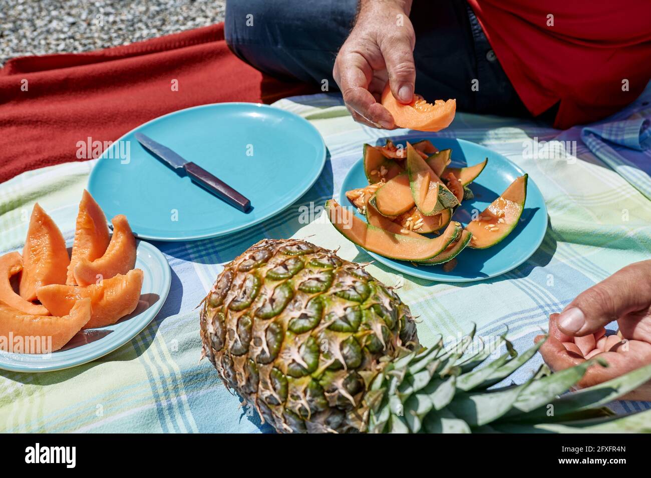 Ehepaar mittleren Alters bei einem Picknick am Meer mit frischen exotischen Früchten. Mann schneidet eine Melone. Frühling, Sommer Lifestyle, Liebe Dating-Konzept. Stockfoto