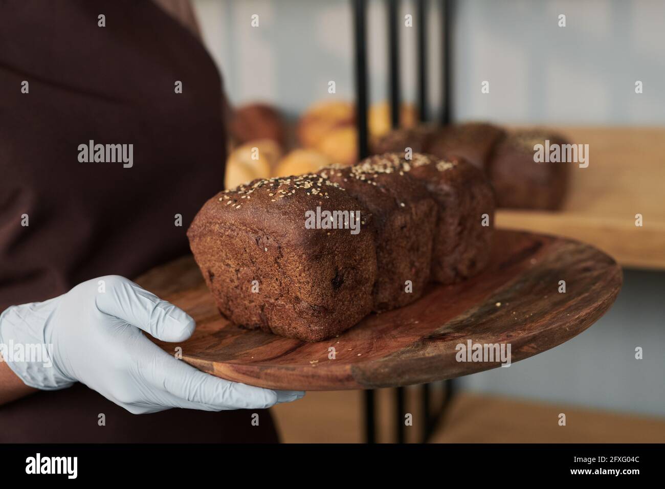 Nahaufnahme einer Frau in Schutzhandschuhen, die ein Holztablett mit hält Hausgemachtes Brot Stockfoto