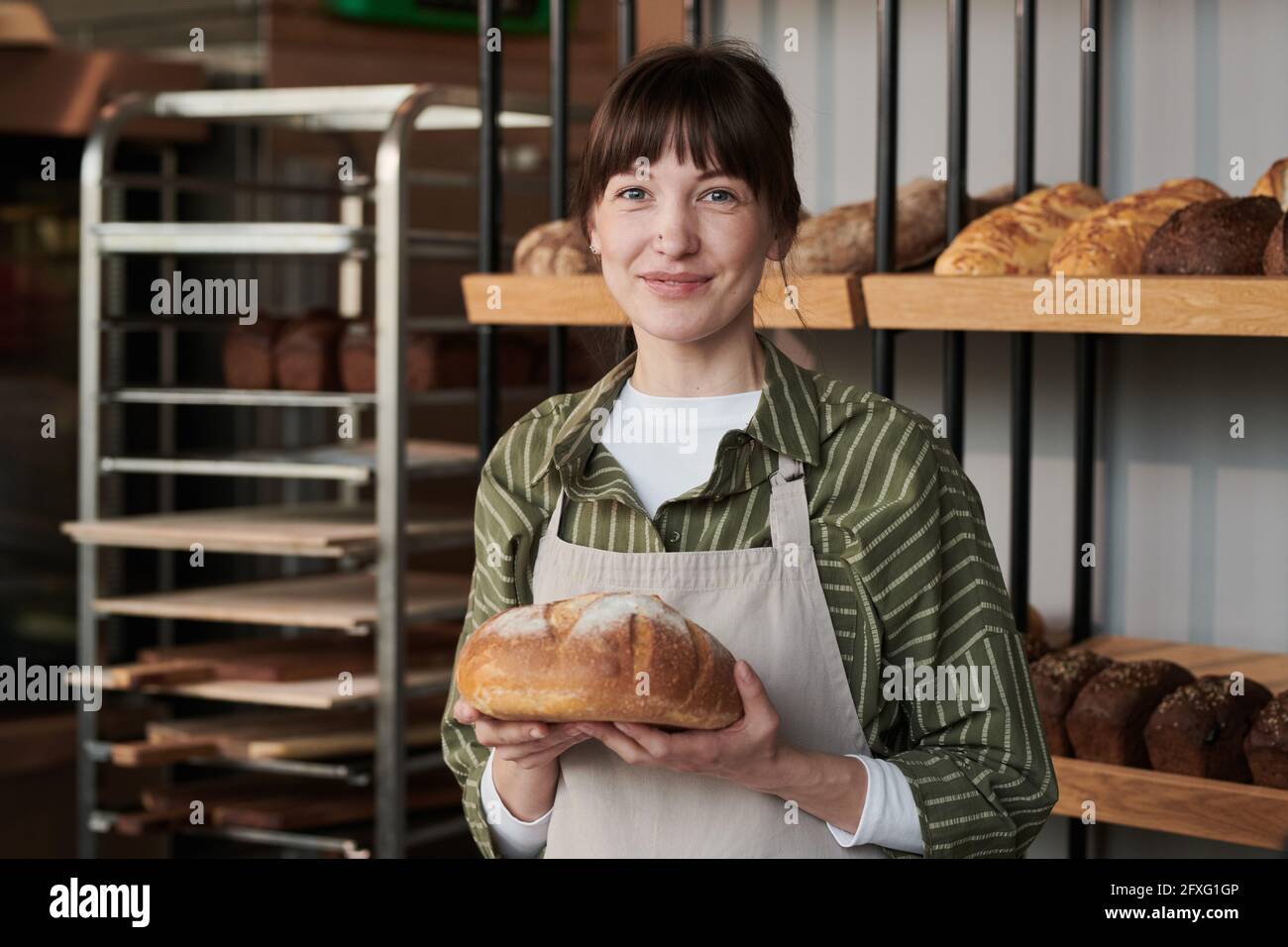 Porträt einer jungen Frau in Schürze mit frischem Brot suchen Bei der Kamera in der Bäckerei Stockfoto