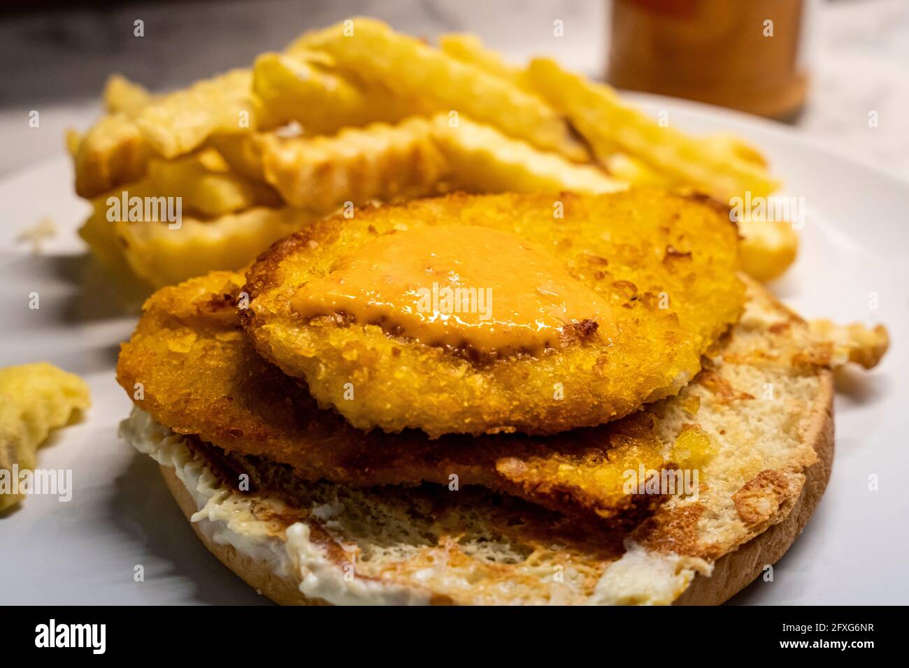 Peri-Peri-Sauce auf einem panierten Hühnchen-Schnitzel, auf einem offenen Brötchen sitzend, mit Käse geröstet, mit knuspriigen Pommes im Hintergrund Stockfoto