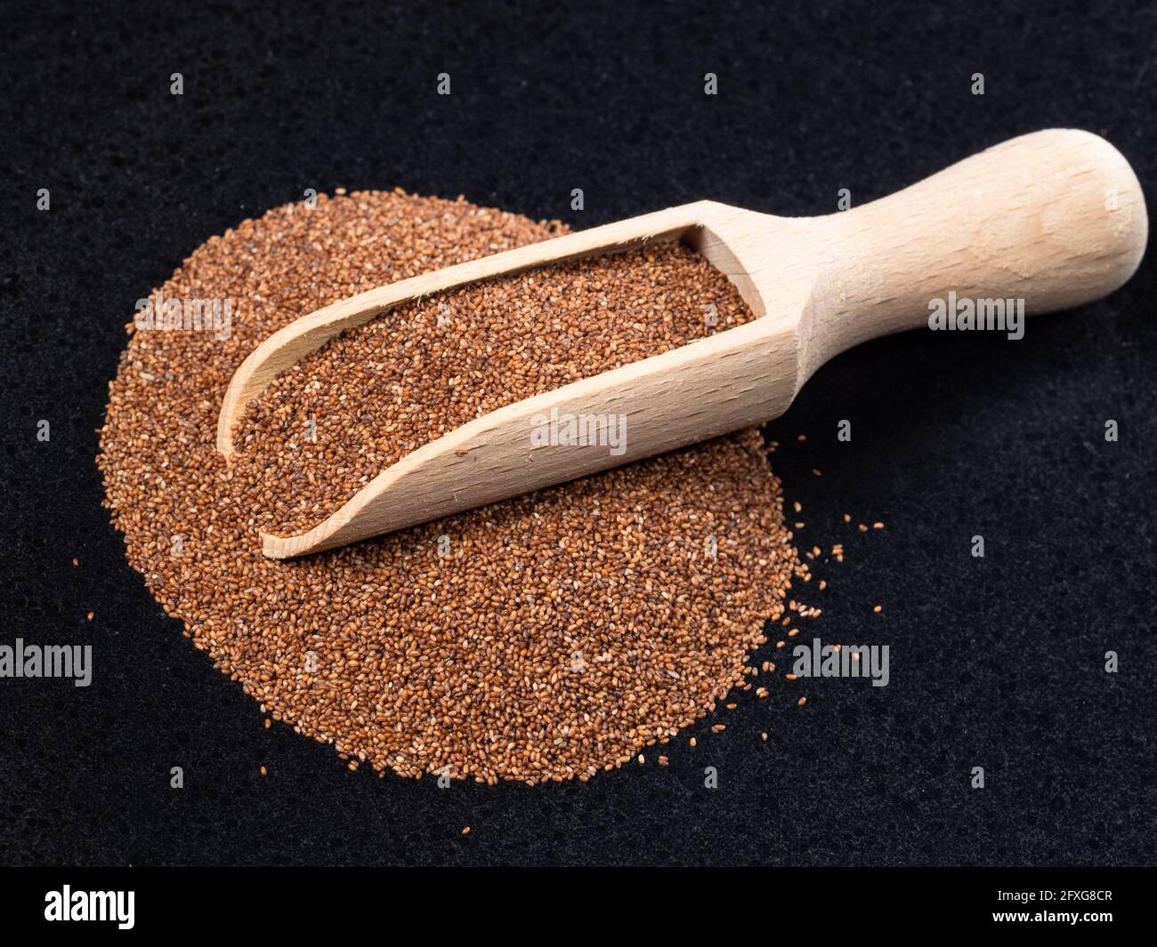 Holzlöffel auf Stapel von Vollkorntaufelsamen auf schwarz Platte Stockfoto