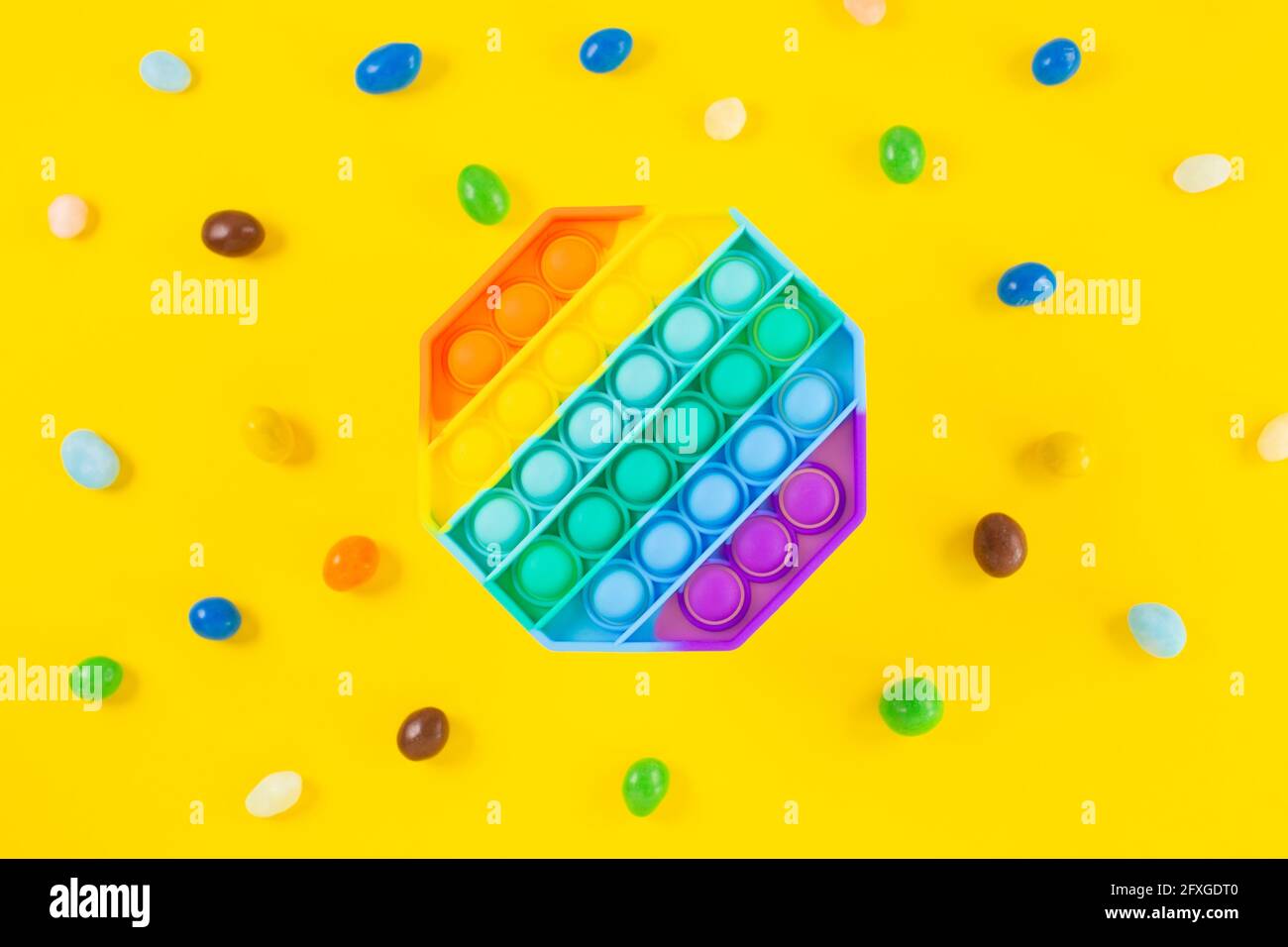 Regenbogen Silikon sensorische Antistress Pop es Spielzeug um bunte Süßigkeiten auf gelbem Hintergrund. Neue beliebte trendige Silikon-Spielzeug. Stockfoto