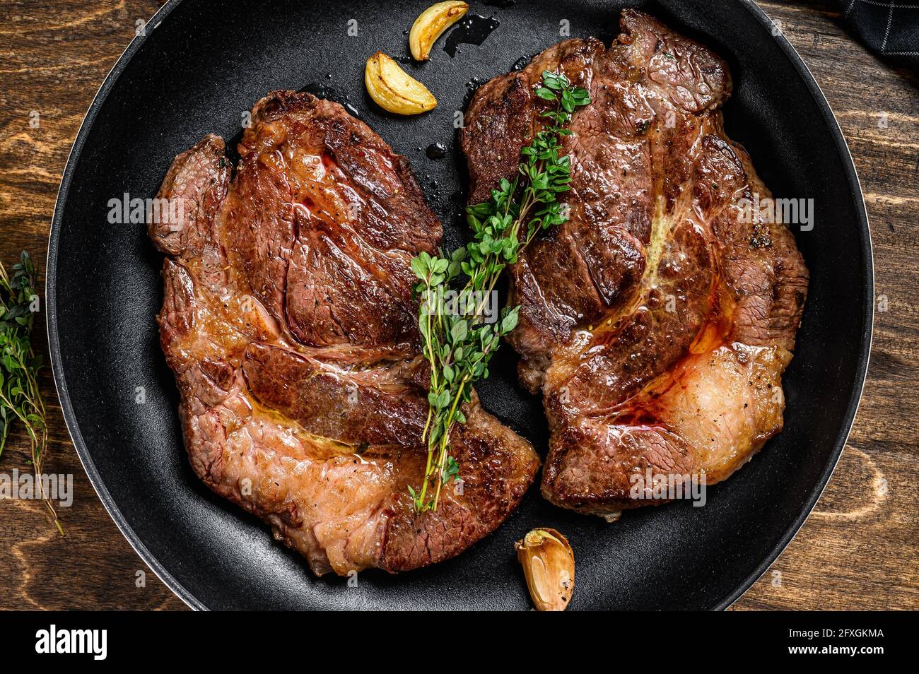 Geröstete Rib Eye Steaks in einer Pfanne. Dunkler Holzhintergrund. Draufsicht Stockfoto