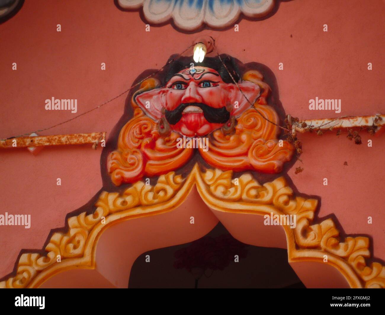 Schnitzerei eines pinkfarbenen wütenden Hindu-gottes mit einem Schnurrbart am Eingang eines Tempels Stockfoto