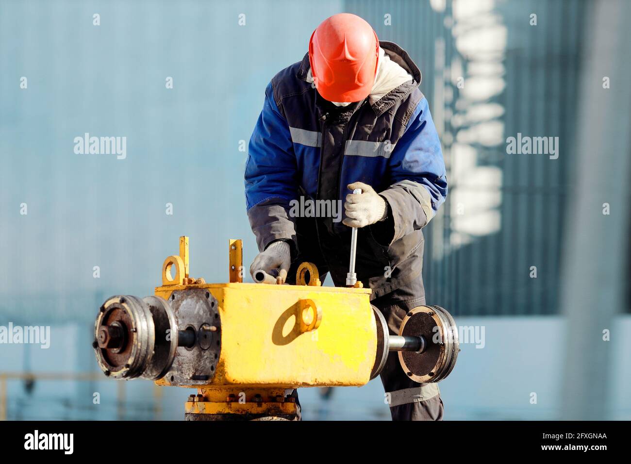 Ein Gasdienstmitarbeiter in Helm und Erbsenjacke bedient eine Kranmontage auf der Straße. Reparatur von Gasanlagen Stockfoto