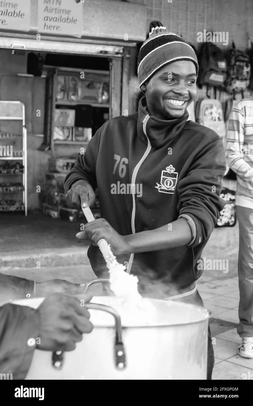 JOHANNESBURG, SÜDAFRIKA - 05. Januar 2021: Johannesburg, Südafrika, 12. Juli 2009, Junger afrikanischer Mann kocht Mielie Pap Maisbrei auf der Seite stre Stockfoto