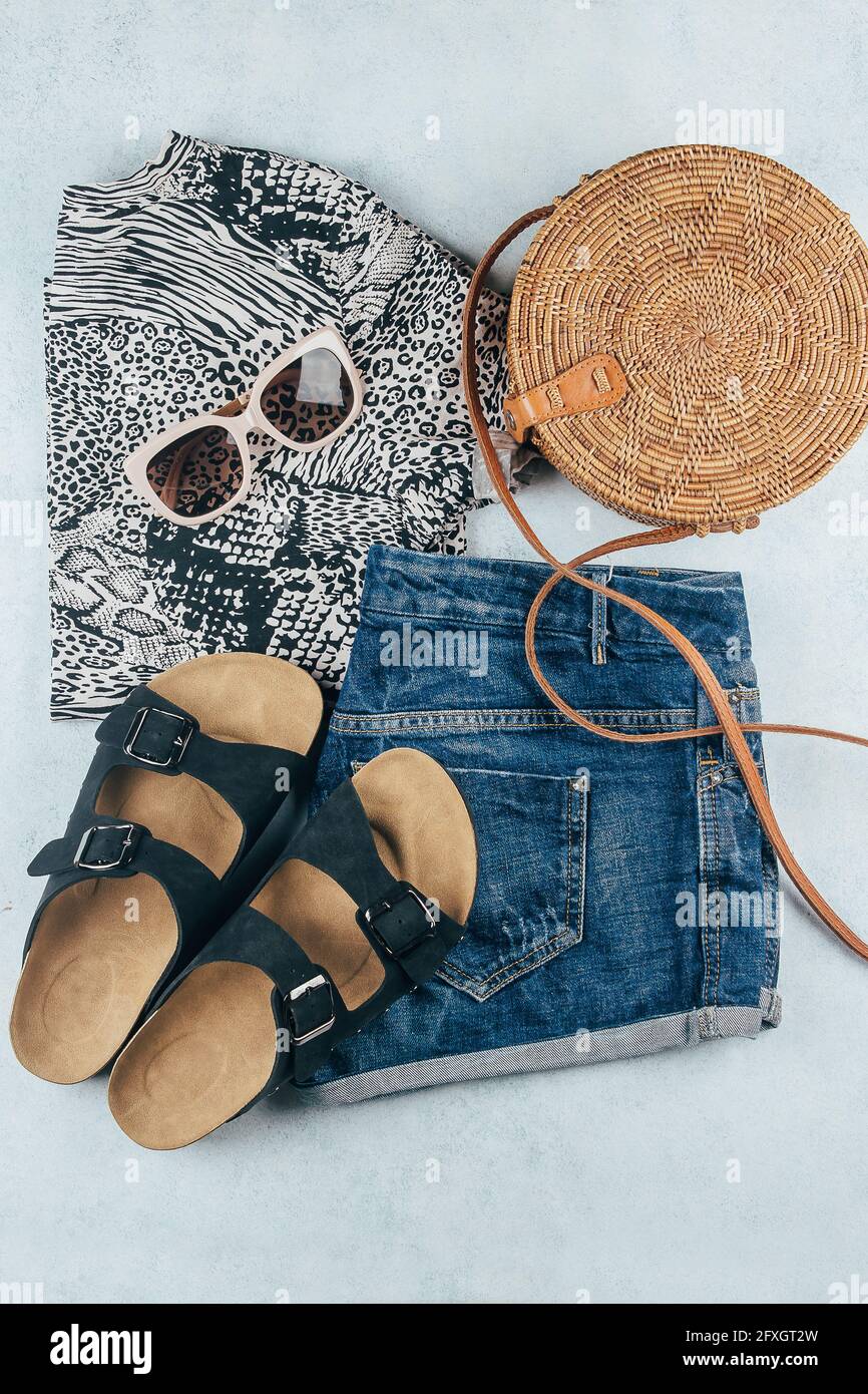 Flaches Lay mit sommerlicher Damenbekleidung und Accessoires. T-Shirt mit Tierdruck, blaue Denim-Shorts, modische Bio-Rattan-Tasche, Sonnenbrille. Urlaub, Stockfoto