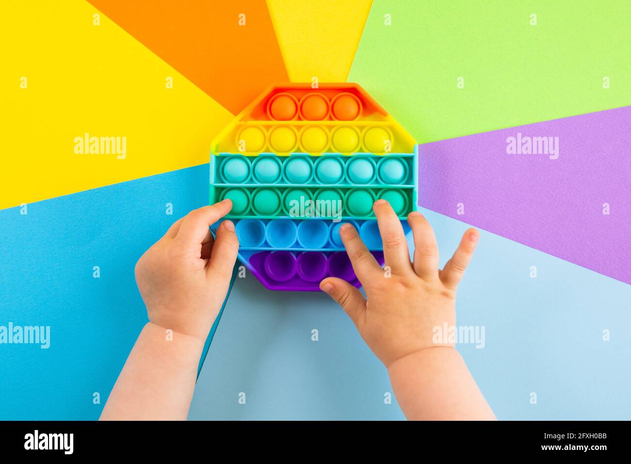 Kinder Hände schieben sensorische popit auf bunten Hintergrund. Antistress-Pop-it-Spielzeug. Rainbow Silikon sensorische Fidget Neue beliebte trendige Silikon-Spielzeug. Stockfoto