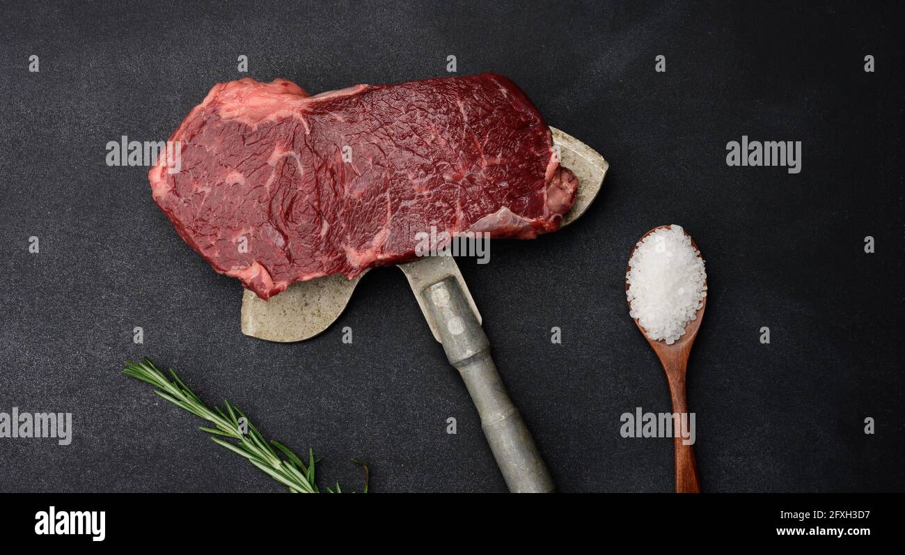 Rohes Stück Rindersteak liegen auf einem Eisenmesser, schwarzer Hintergrund. Klassisches Steak, Blick von oben Stockfoto