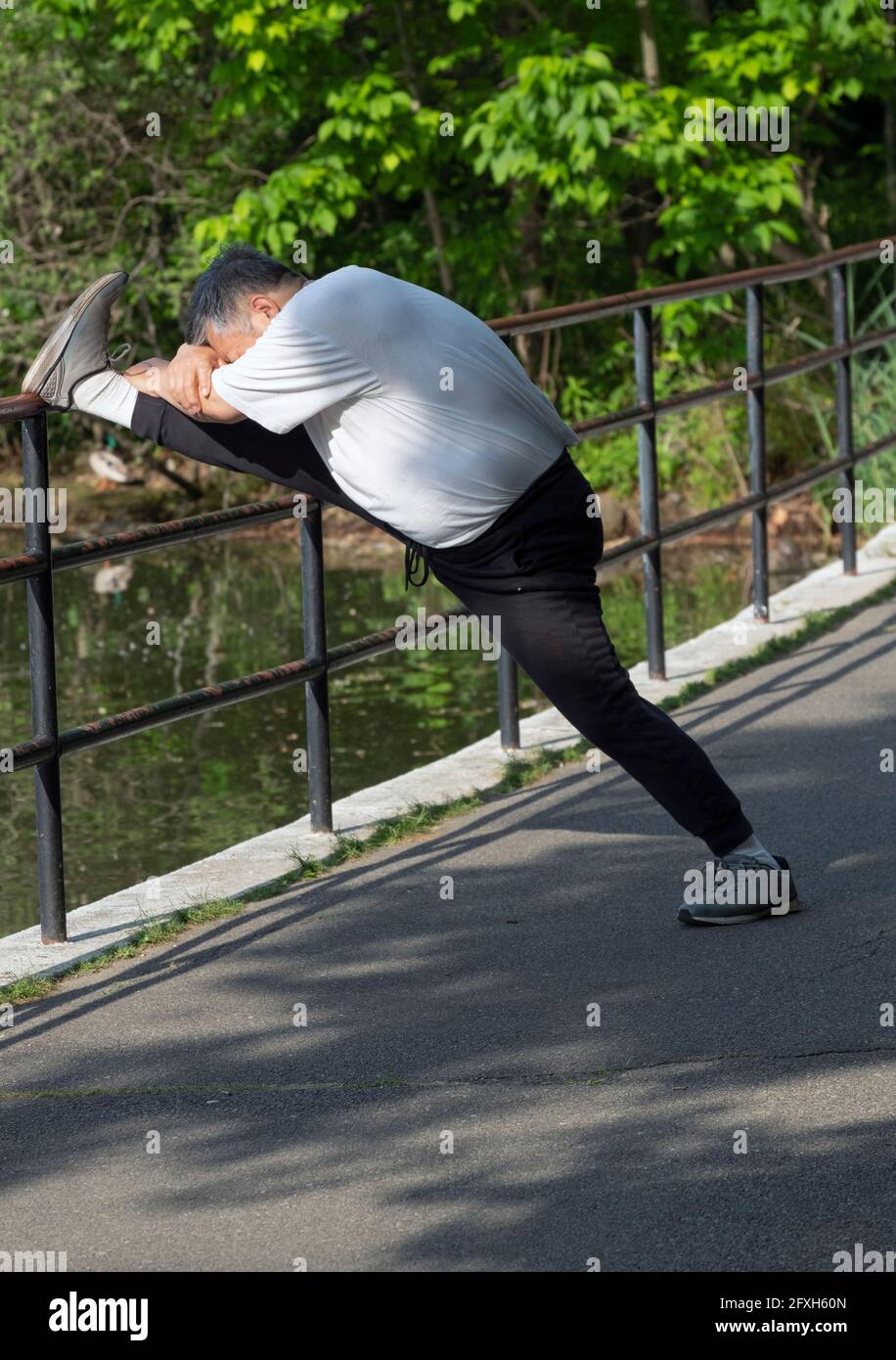 Ein Mann mittleren Alters streckt sein Bein in einem Park in Queens, New York City. Stockfoto