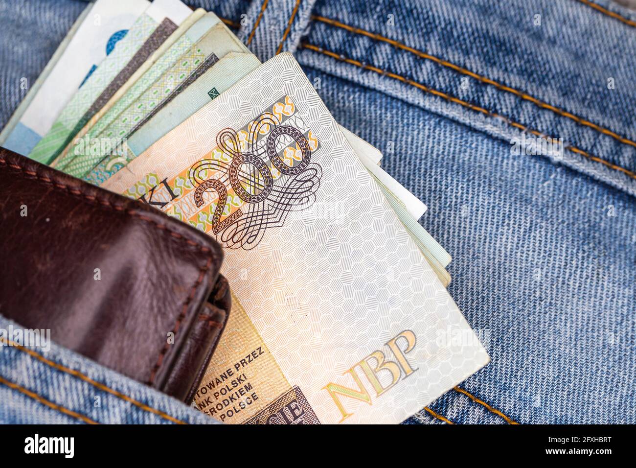 Brieftasche und viele polnische Banknoten ragen aus der Gesäßtasche der Denim-Hose. Foto aufgenommen unter künstlichem, weichem Licht Stockfoto