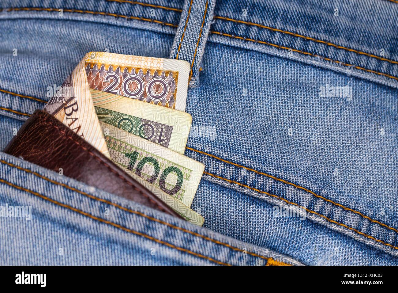 Brieftasche und viele polnische Banknoten ragen aus der Gesäßtasche der Denim-Hose. Foto aufgenommen unter künstlichem, weichem Licht Stockfoto