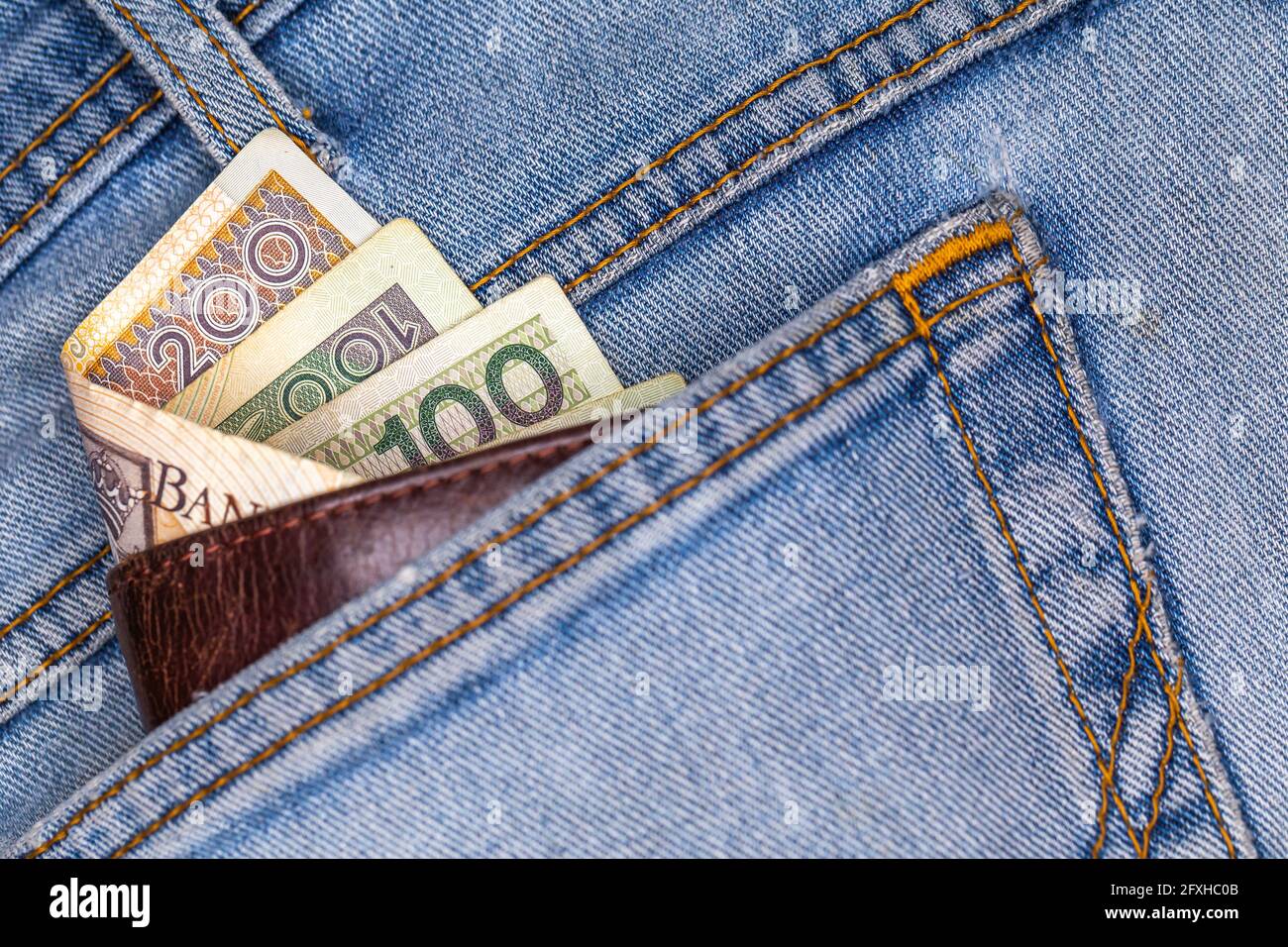 Brieftasche und viele polnische Banknoten ragen aus der Gesäßtasche der Denim-Hose. Foto aufgenommen unter künstlichem, weichem Licht Stockfoto