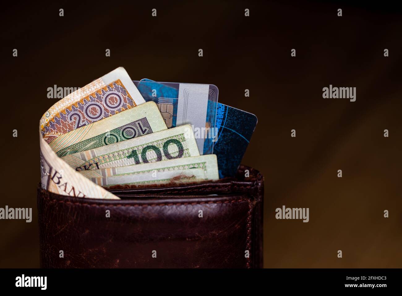 Viele polnische Banknoten und Kreditkarten ragen aus einer braunen Ledertasche. Foto aufgenommen unter künstlichem, weichem Licht Stockfoto