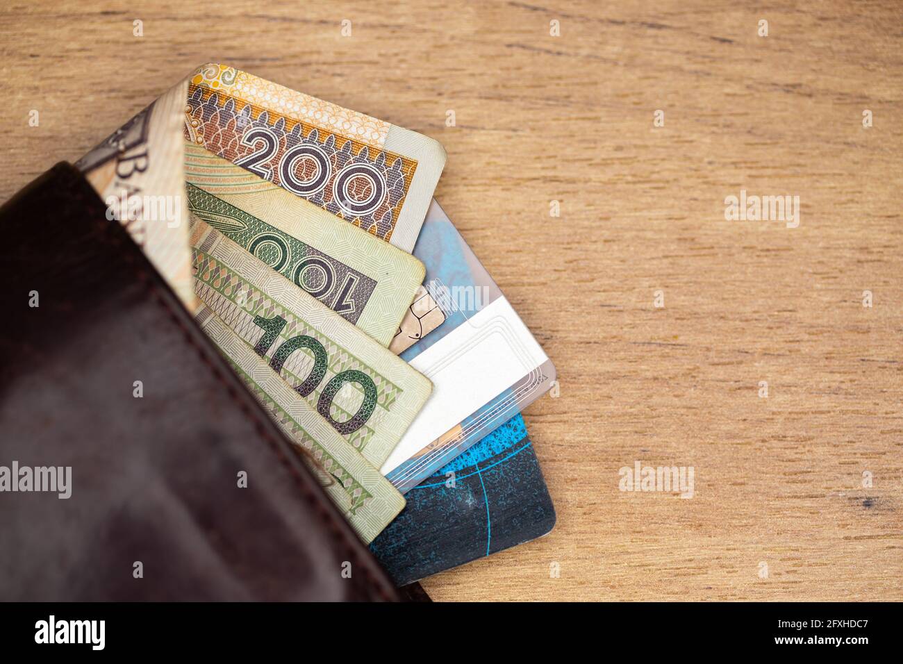 Viele polnische Banknoten und Kreditkarten ragen aus einer braunen Ledertasche. Foto aufgenommen unter künstlichem, weichem Licht Stockfoto