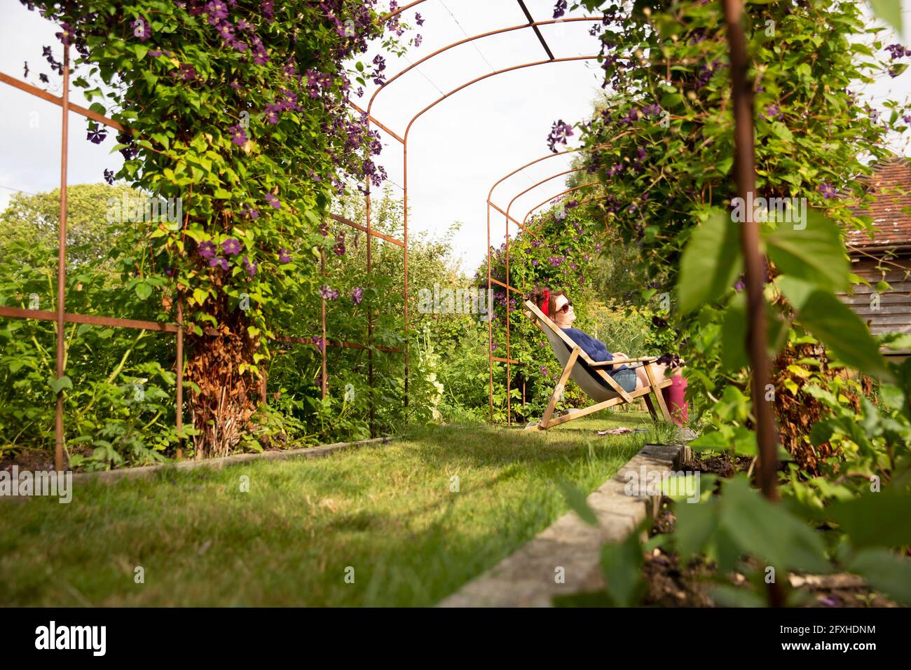 Ruhige Frau, die sich im Liegesessel im sonnigen Sommergarten entspannt Stockfoto