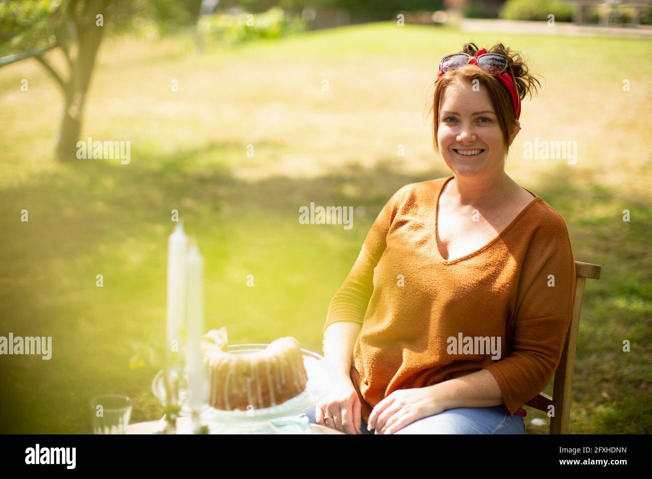 Portrait glückliche Frau, die Kuchen am Tisch im sonnigen Sommergarten genießt Stockfoto