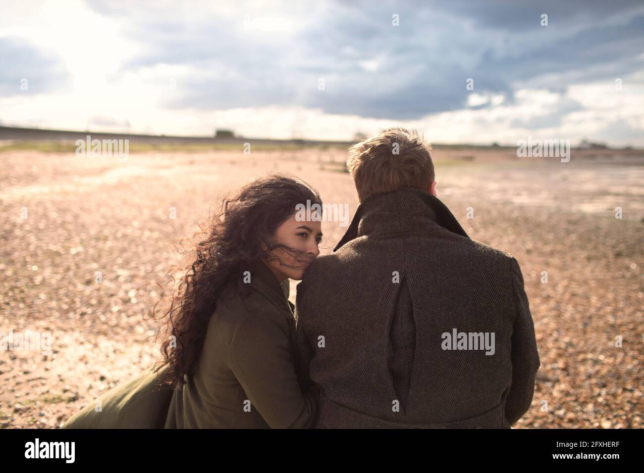 Paar in Mänteln am sonnigen, windigen Winterstrand Stockfoto