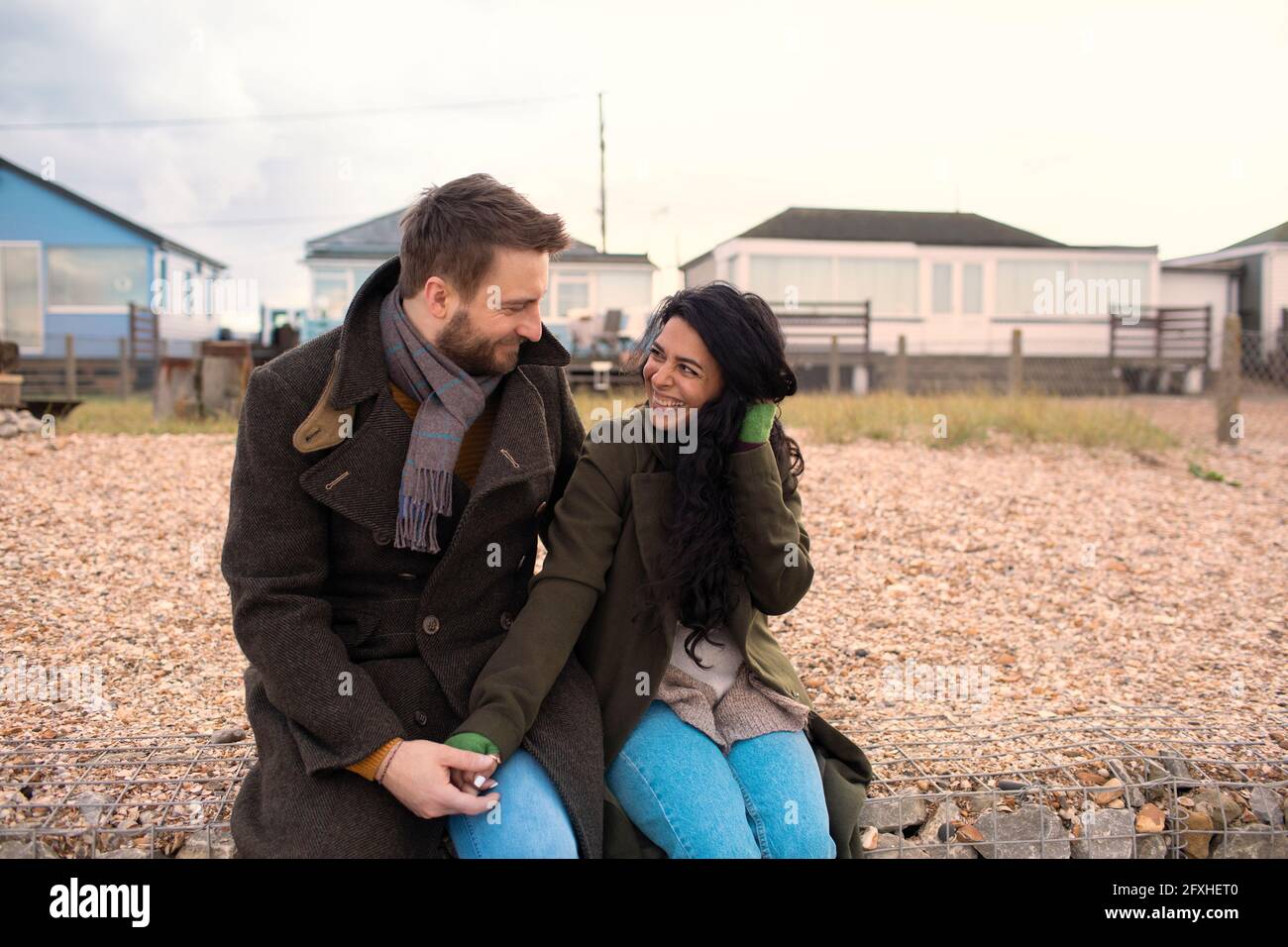 Glückliches Paar in Wintermänteln vor Strandhäusern Stockfoto