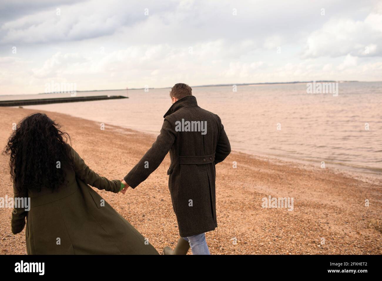 Zärtliches Paar, das sich die Hände hält und am Strand des Wintermeers läuft Stockfoto