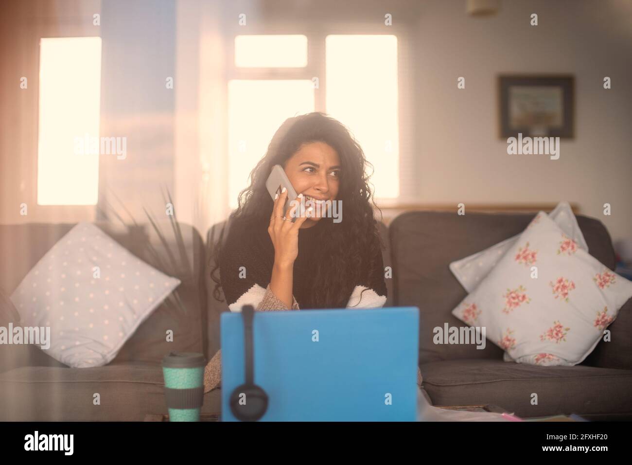 Lächelnde Frau, die von zu Hause aus mit einem Smartphone am Laptop spricht Stockfoto
