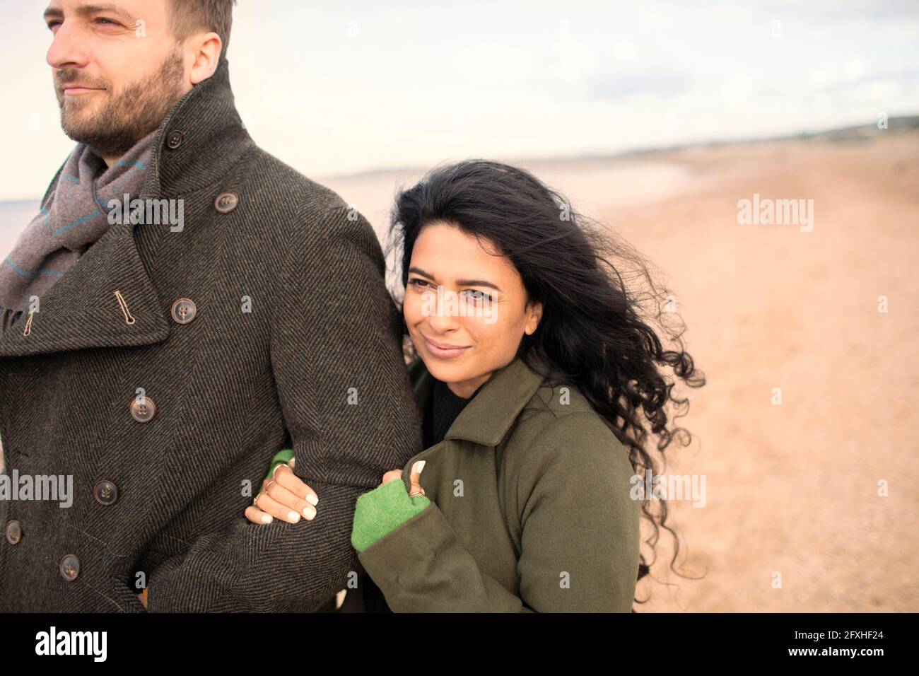 Glückliches Paar in Wintermänteln am Strand Stockfoto