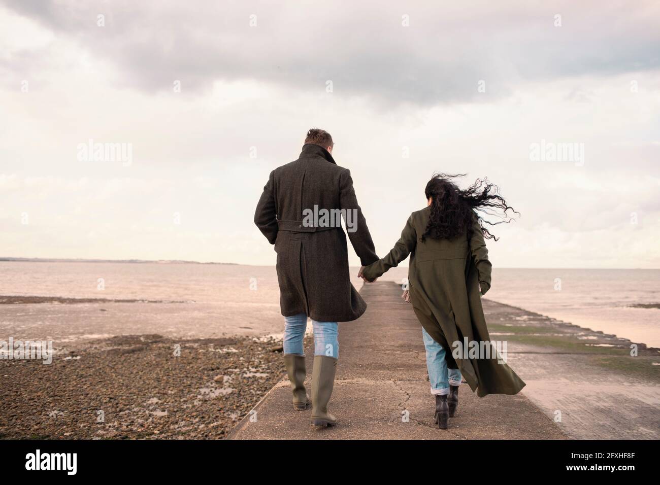 Paar in Wintermänteln, die die Hände am Meeresstrand halten Stockfoto