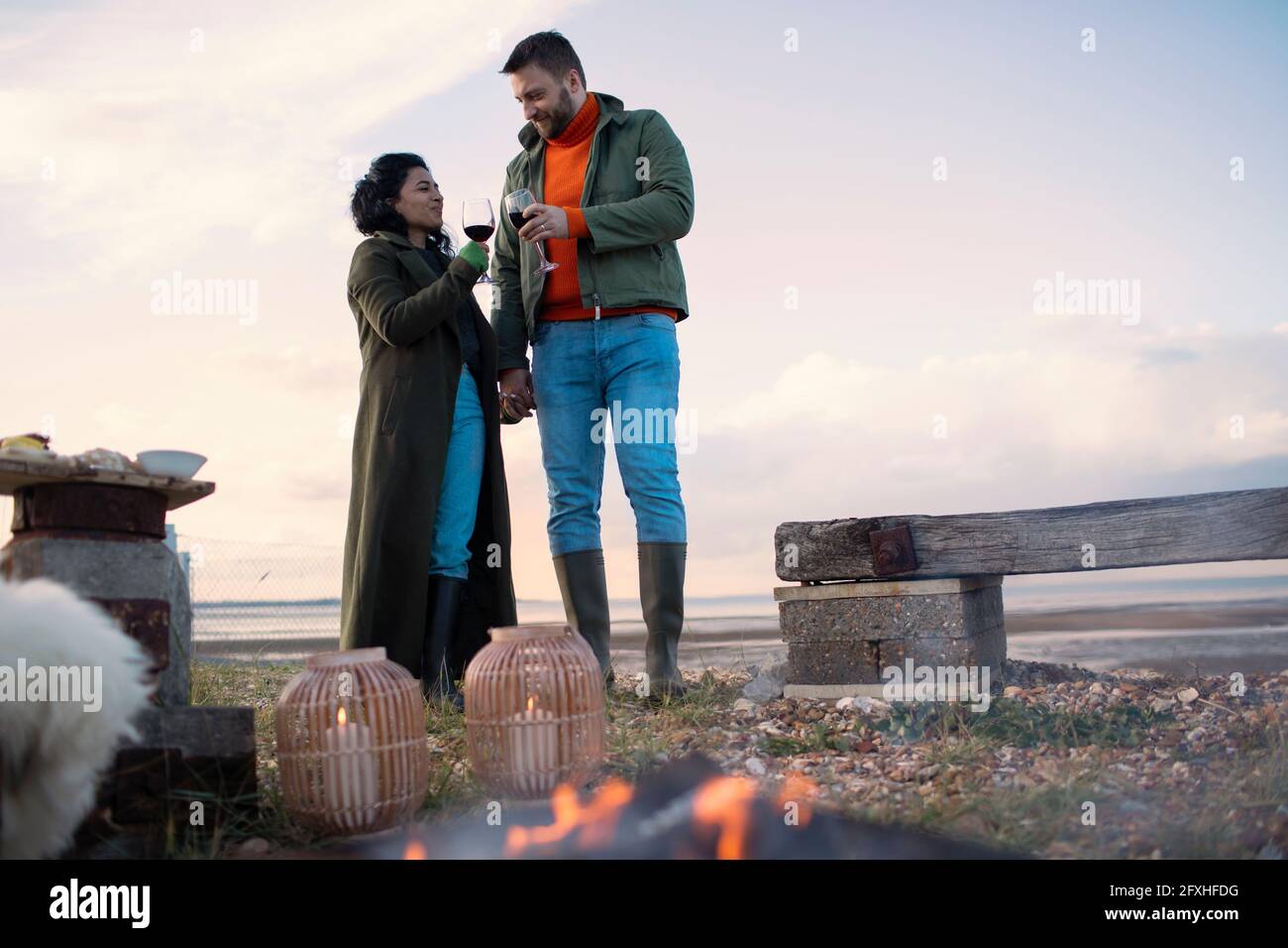 Paar in Wintermänteln genießen Rotwein am Strand Stockfoto