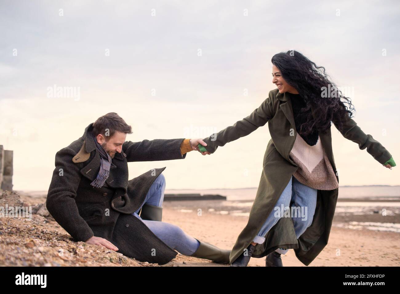 Verspieltes Paar in Wintermänteln am Strand Stockfoto