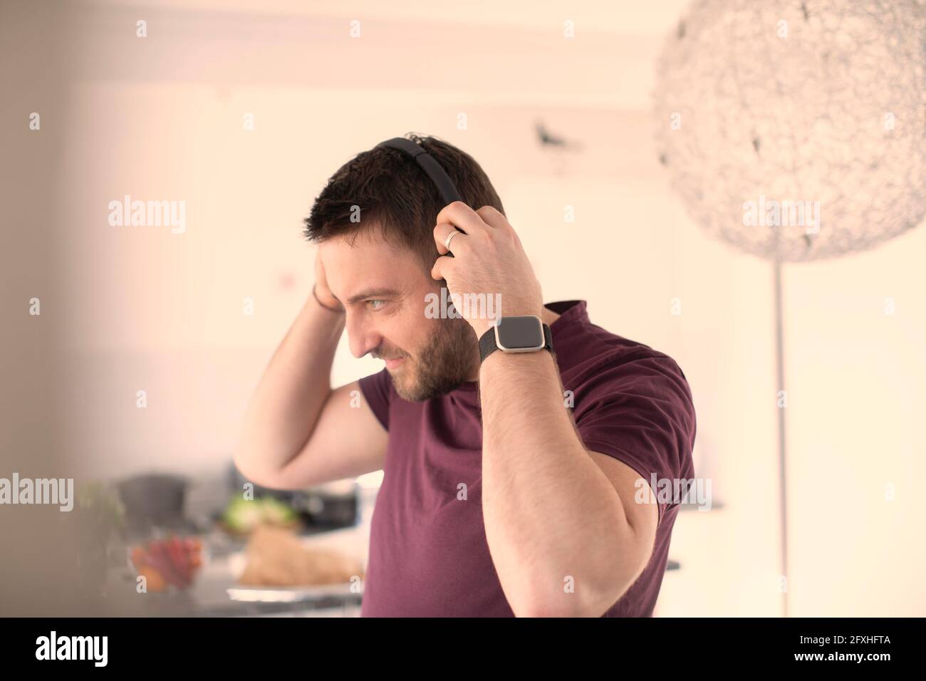 Mann mit smarter Uhr und Kopfhörern, der zu Hause Musik hört Stockfoto