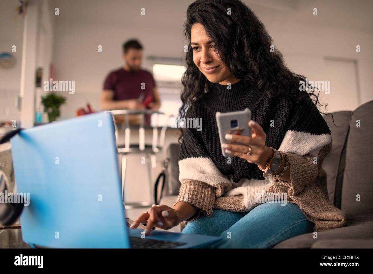 Frau, die von zu Hause aus mit Laptop und Smartphone auf dem Sofa arbeitet Stockfoto
