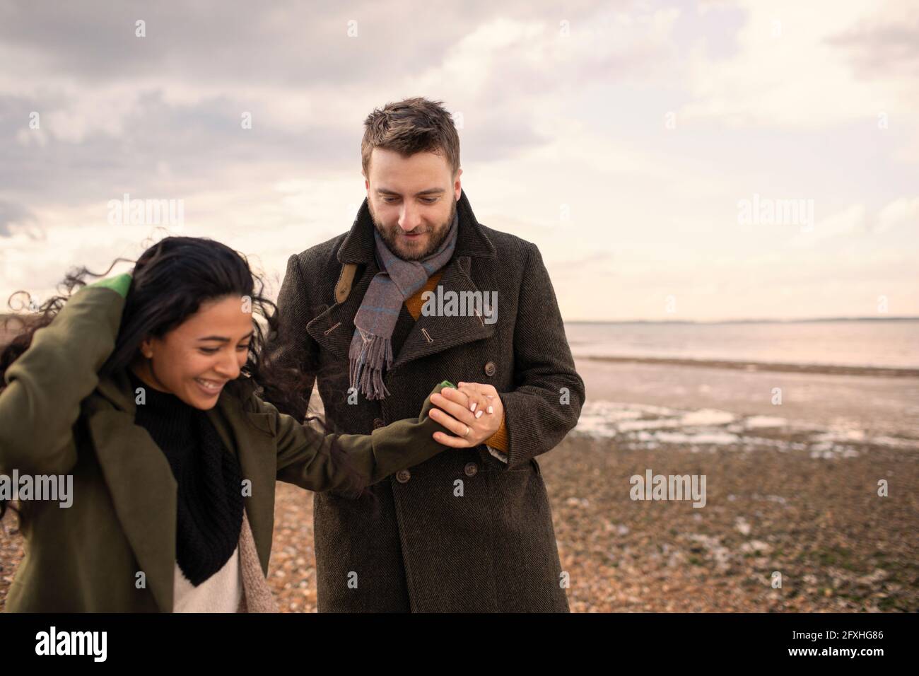 Glückliches Paar in Wintermänteln, das die Hände am Strand hält Stockfoto