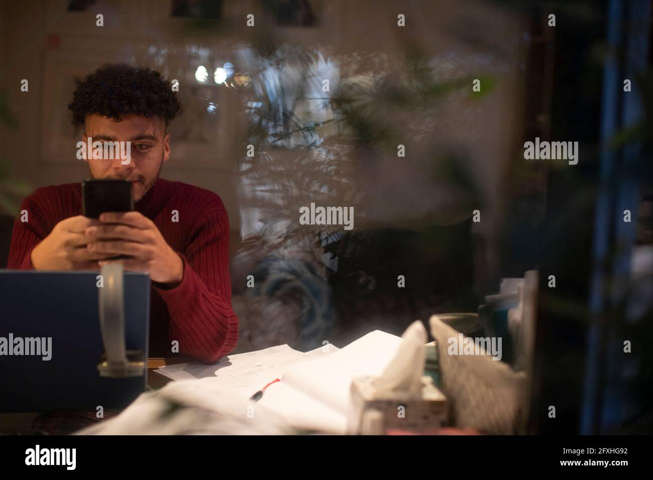 Mann mit Smartphone, der nachts am Laptop im Büro von zu Hause aus arbeitet Stockfoto