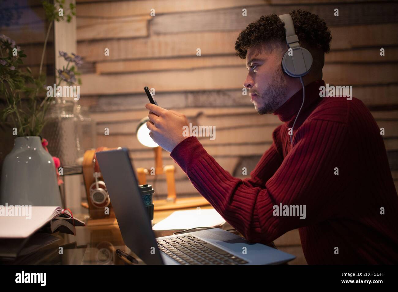Junger Mann mit Kopfhörern, der zu Hause mit Smartphone und Laptop arbeitet Stockfoto