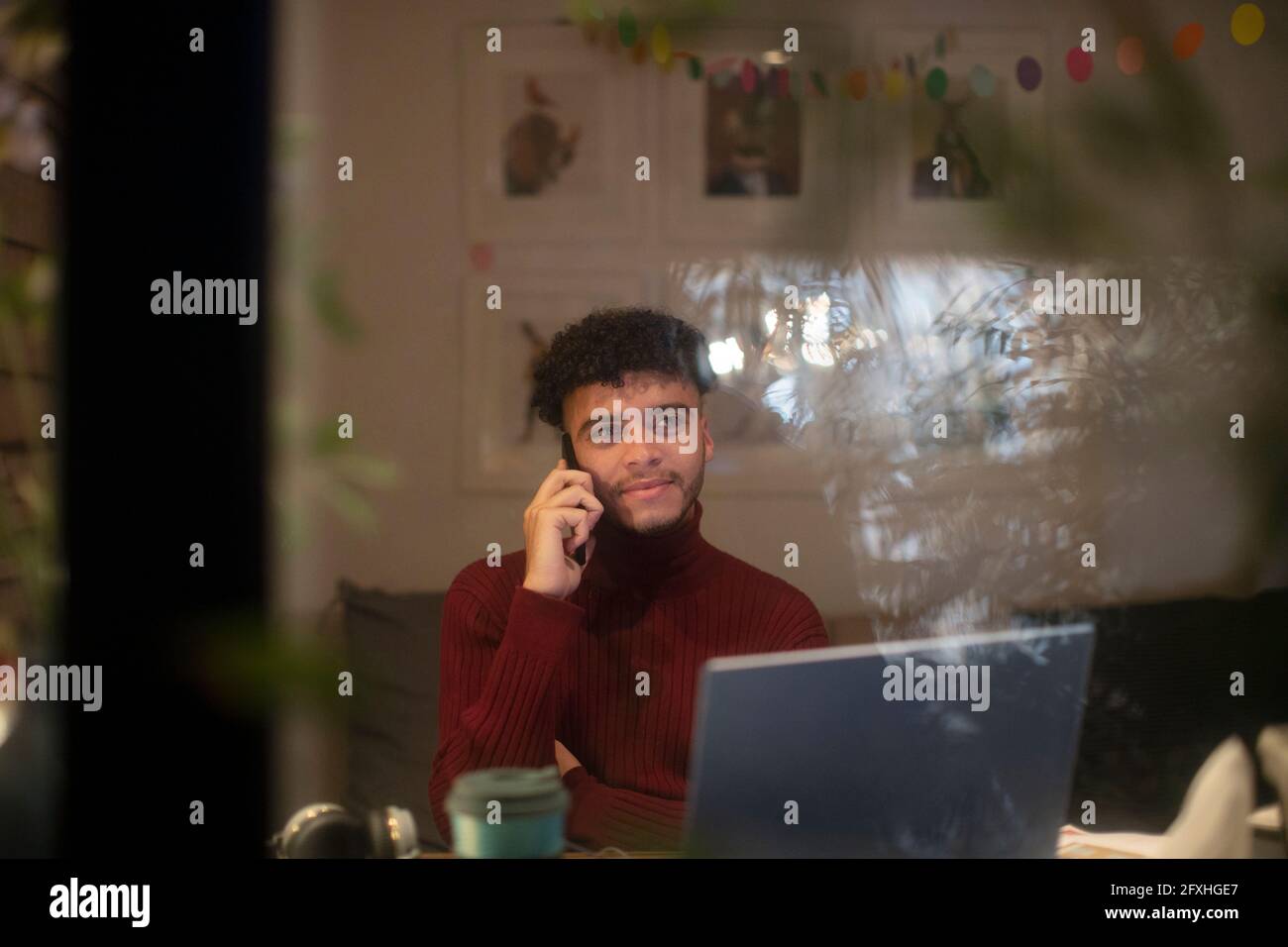 Junger Mann, der von zu Hause aus am Laptop mit einem Smartphone spricht Stockfoto