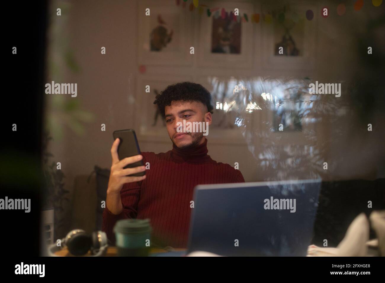 Junger Mann, der von zu Hause aus mit Smartphone und Laptop arbeitet Stockfoto