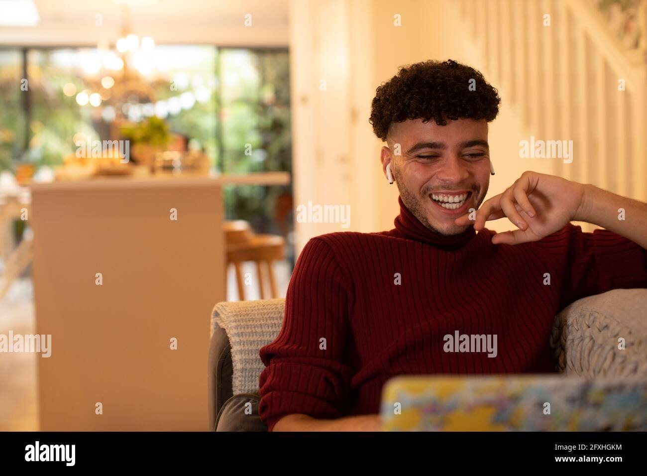 Fröhlicher junger Mann mit Ohrhörern, der sich Filme auf dem Laptop ansieht Stockfoto