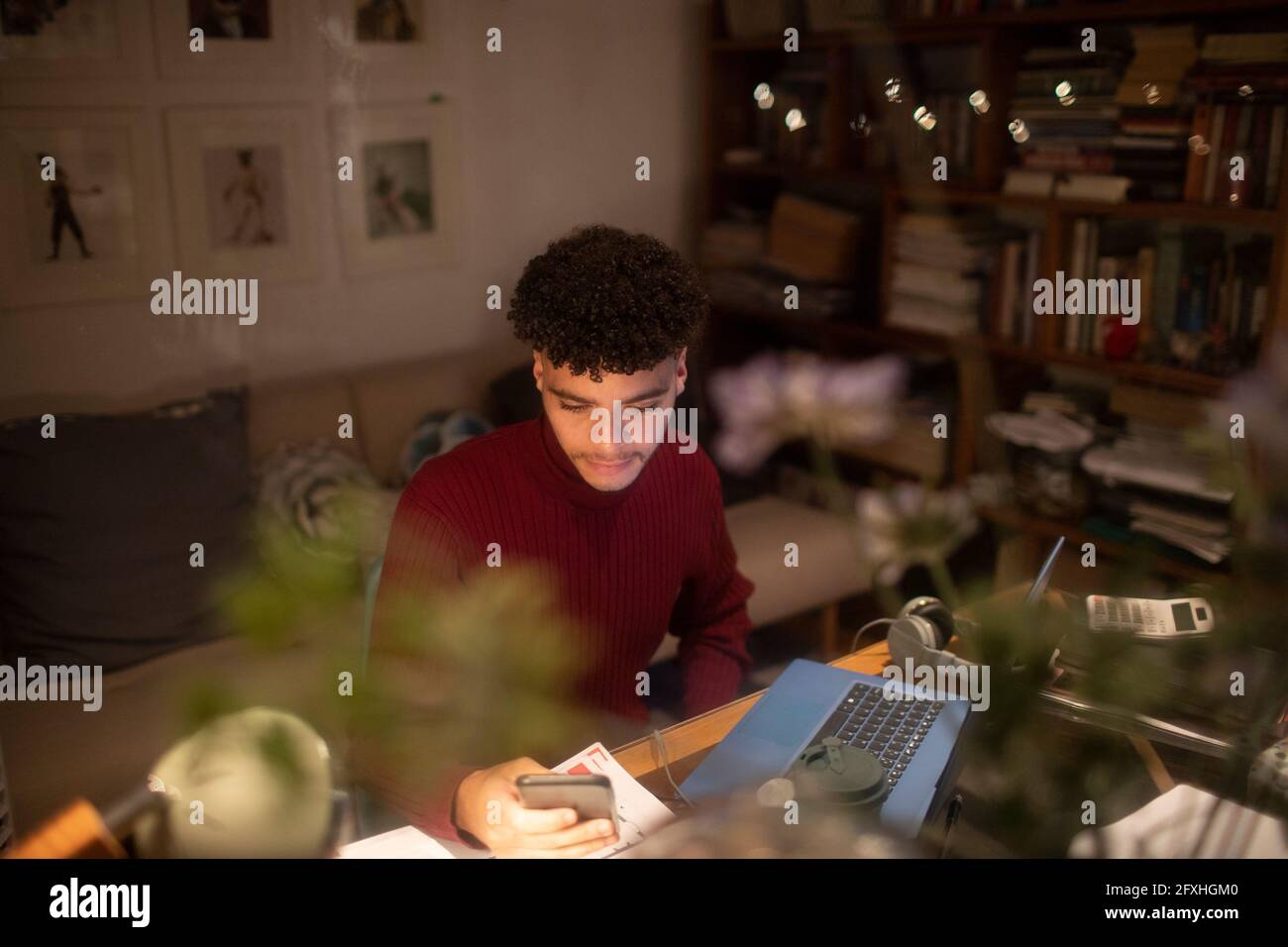 Junger Mann mit Smartphone, der von zu Hause aus am Laptop im Heimbüro arbeitet Stockfoto