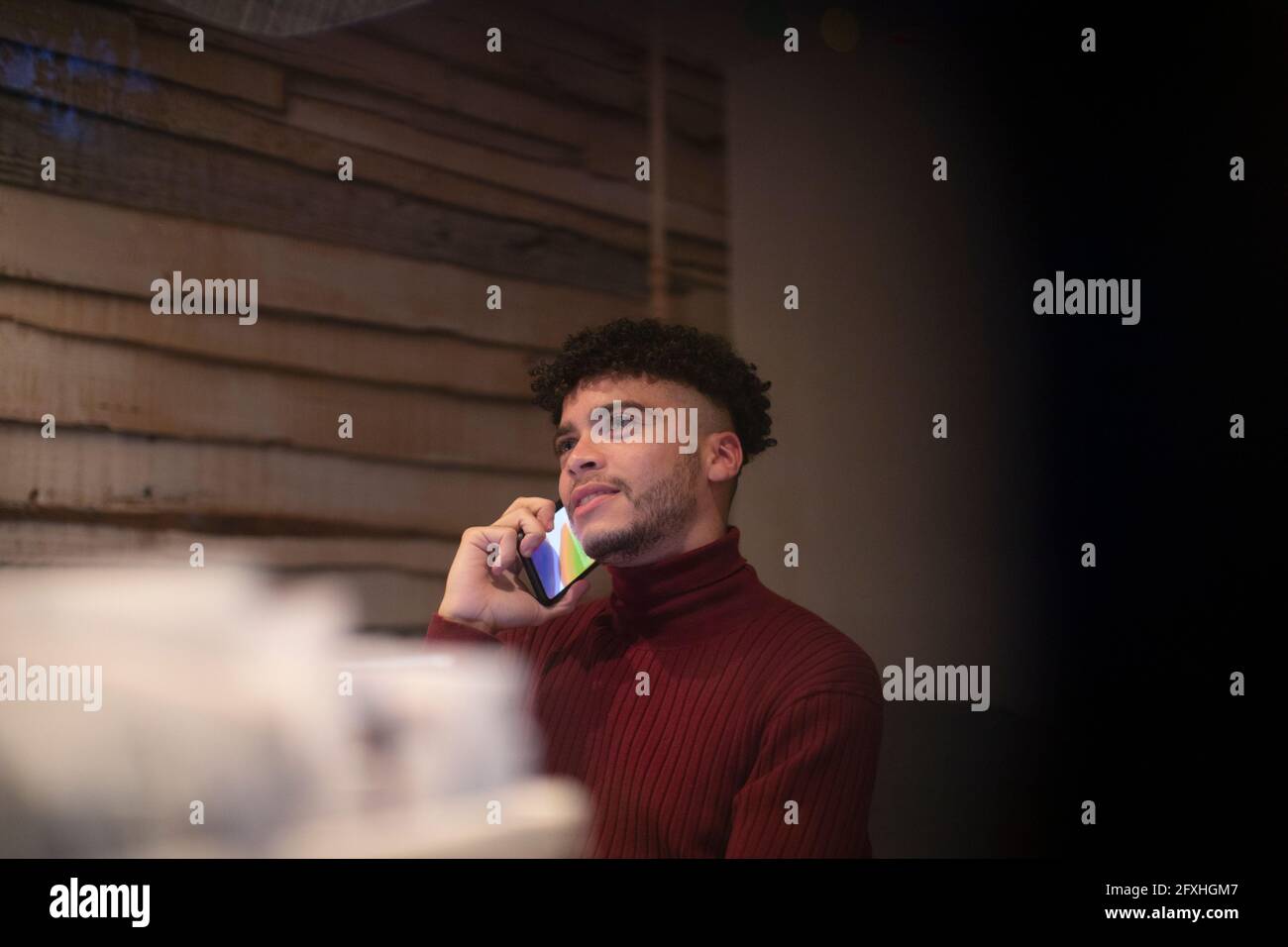 Junger Mann, der im Heimbüro auf dem Smartphone spricht Stockfoto