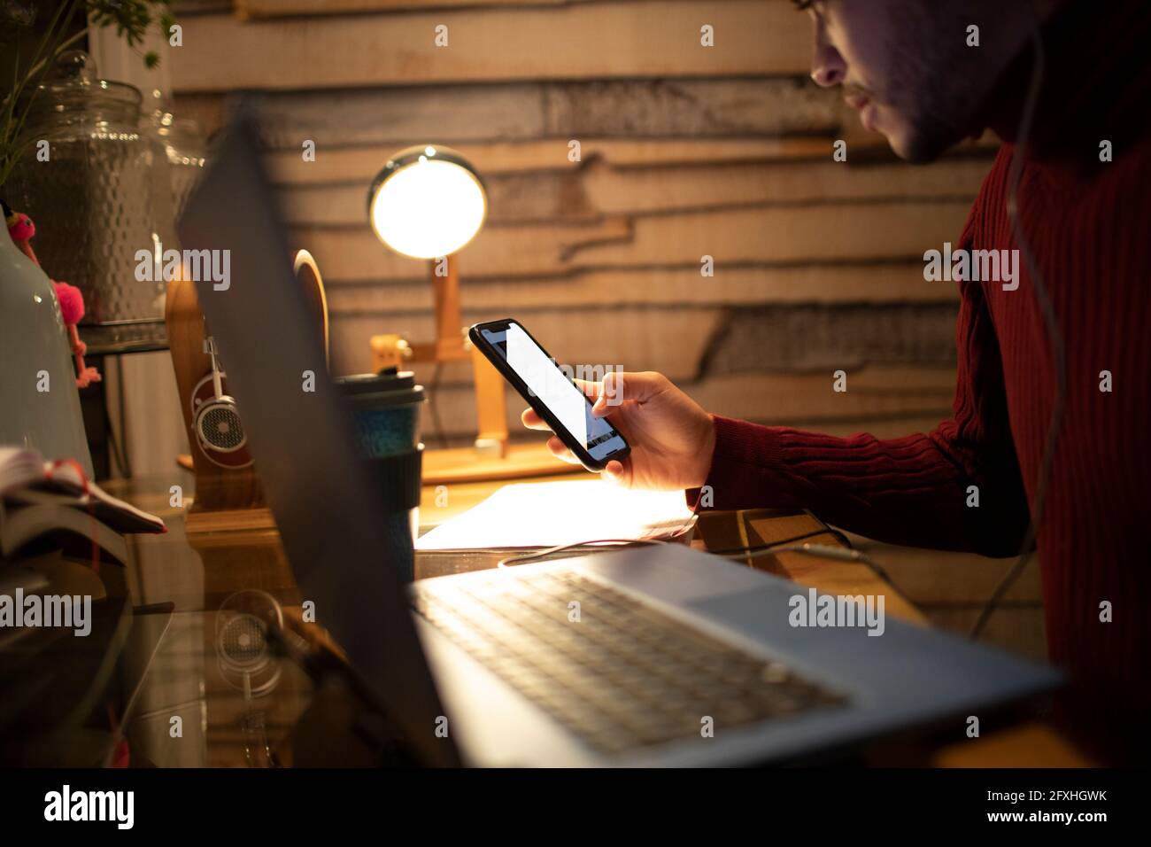 Junger Mann mit Smartphone am Laptop im Heimbüro Stockfoto