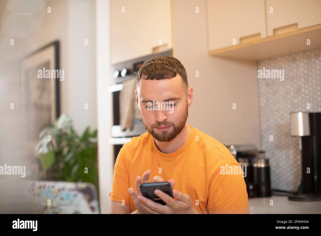 Junger Mann mit Smartphone in der Küche Stockfoto