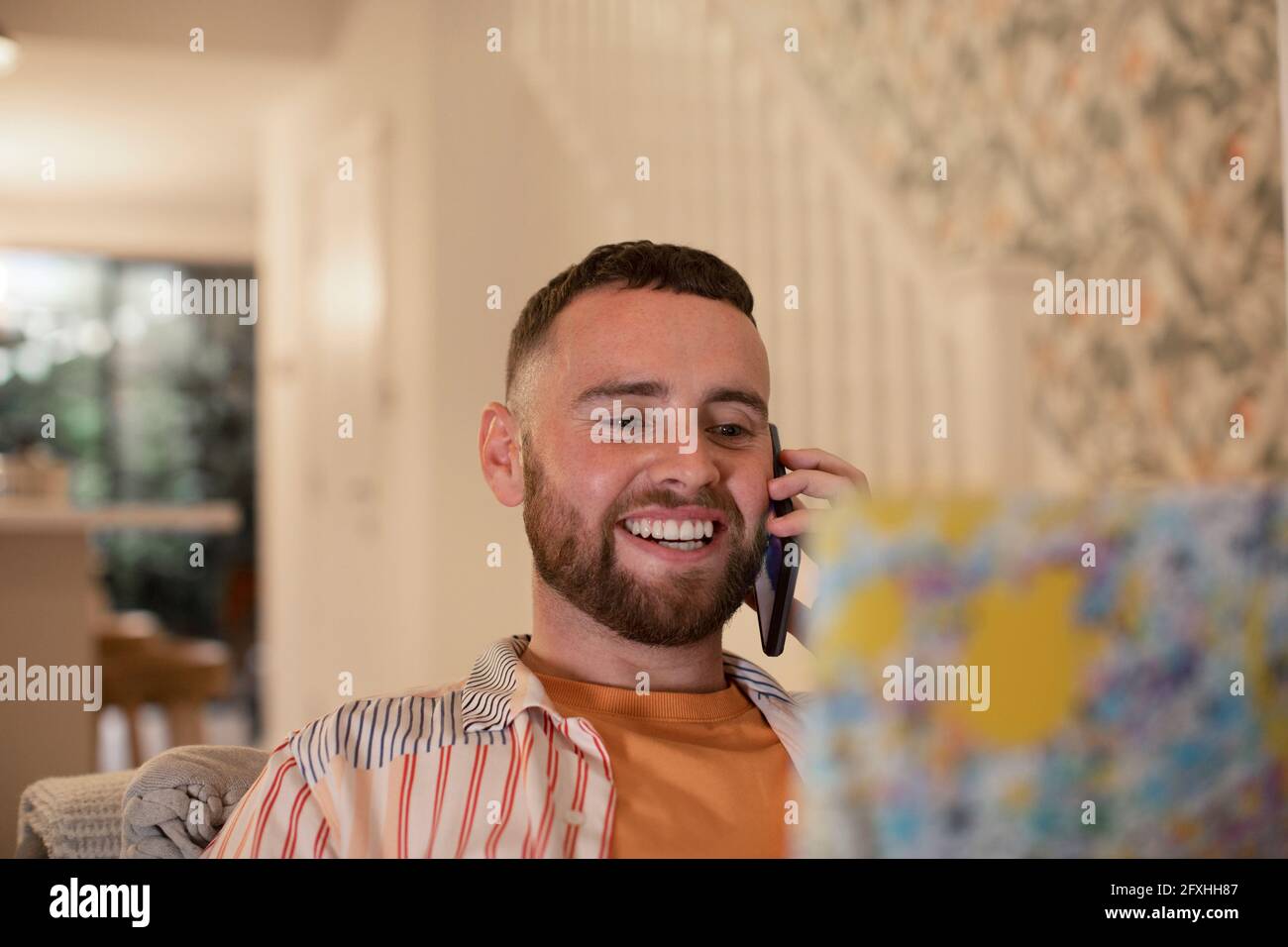 Glücklicher junger Mann, der am Laptop auf dem Smartphone spricht Stockfoto