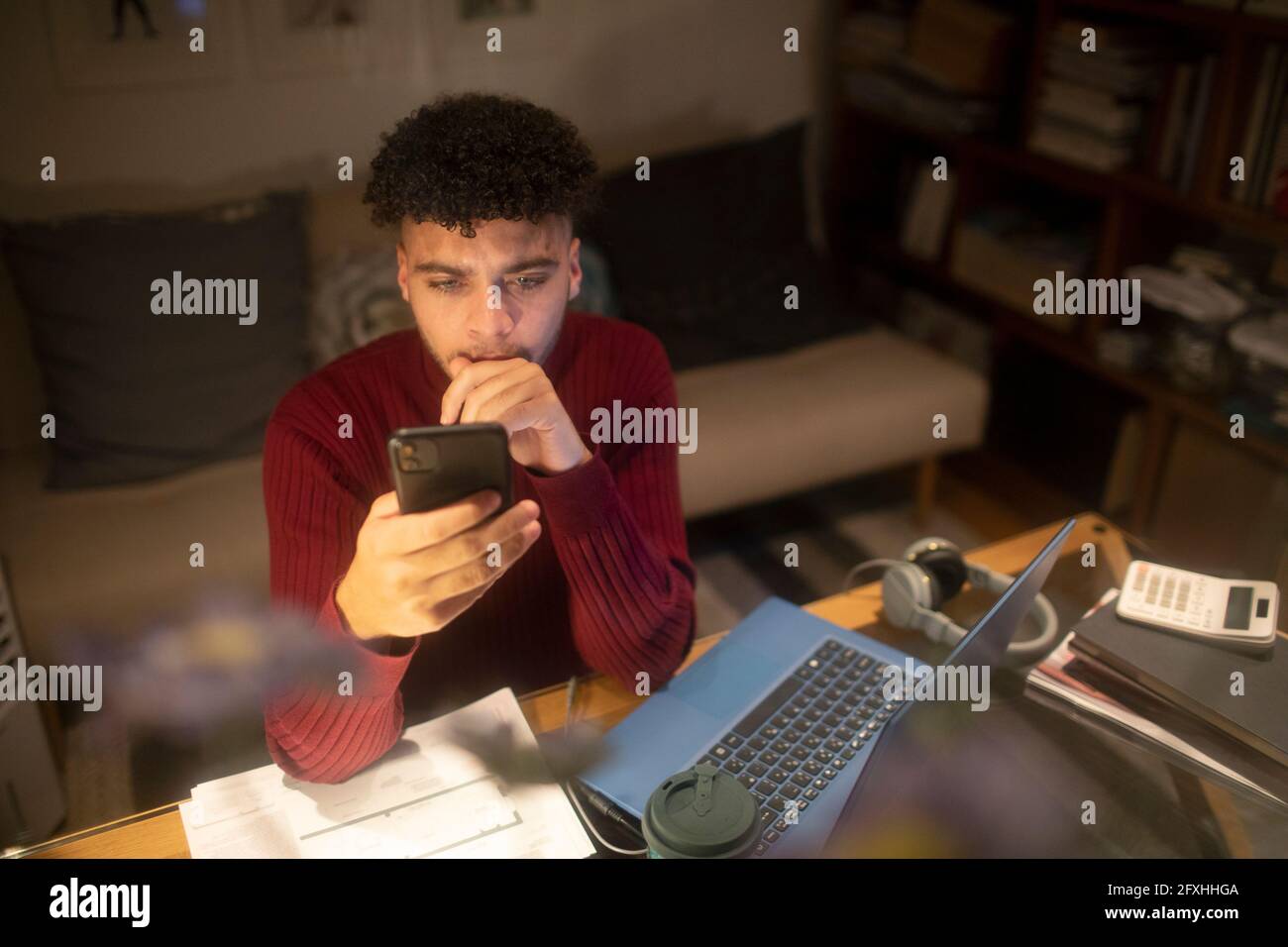 Junger Mann mit Smartphone, der von zu Hause aus am Laptop arbeitet Stockfoto