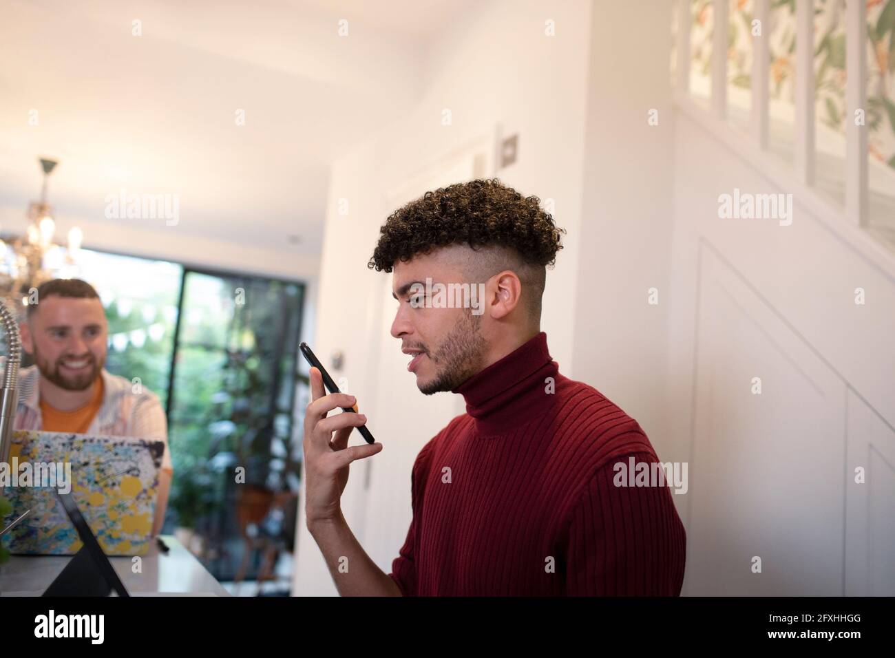 Junger Mann, der in der Küche über einen Smartphone-Lautsprecher spricht Stockfoto
