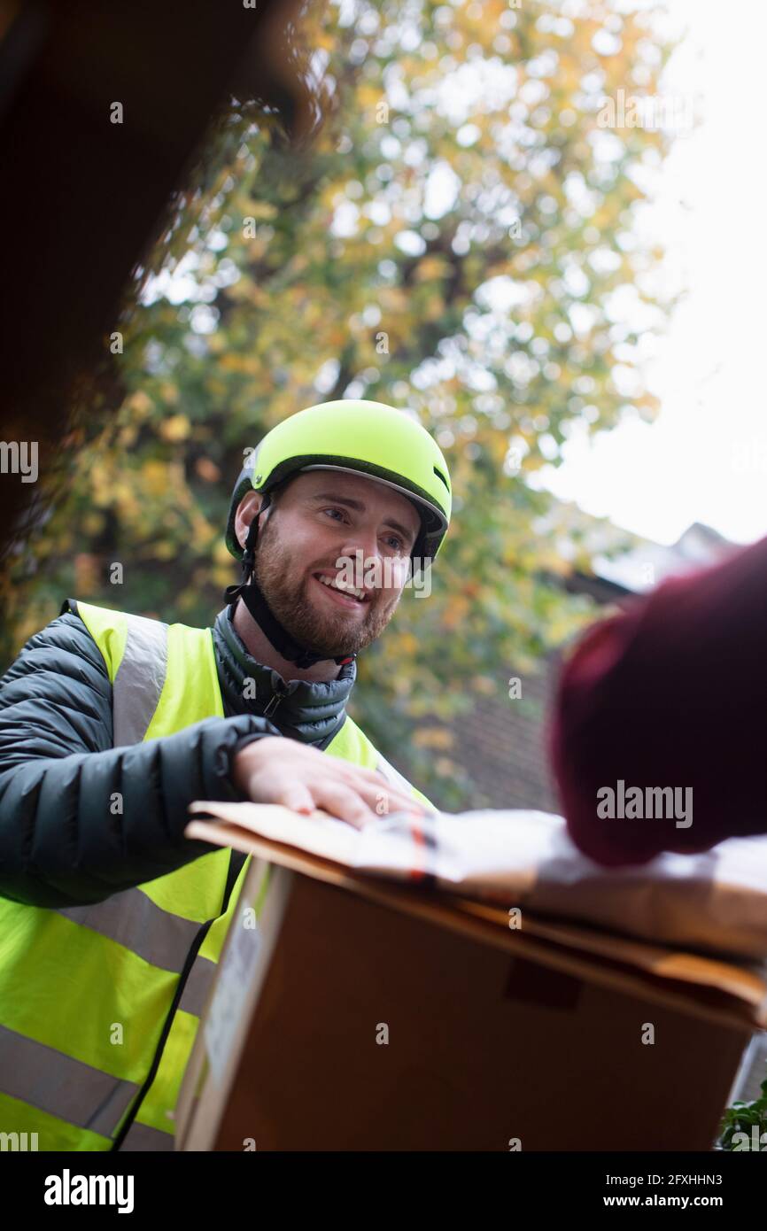 Freundlicher Lieferer im Helm, der Pakete an die Tür liefert Stockfoto