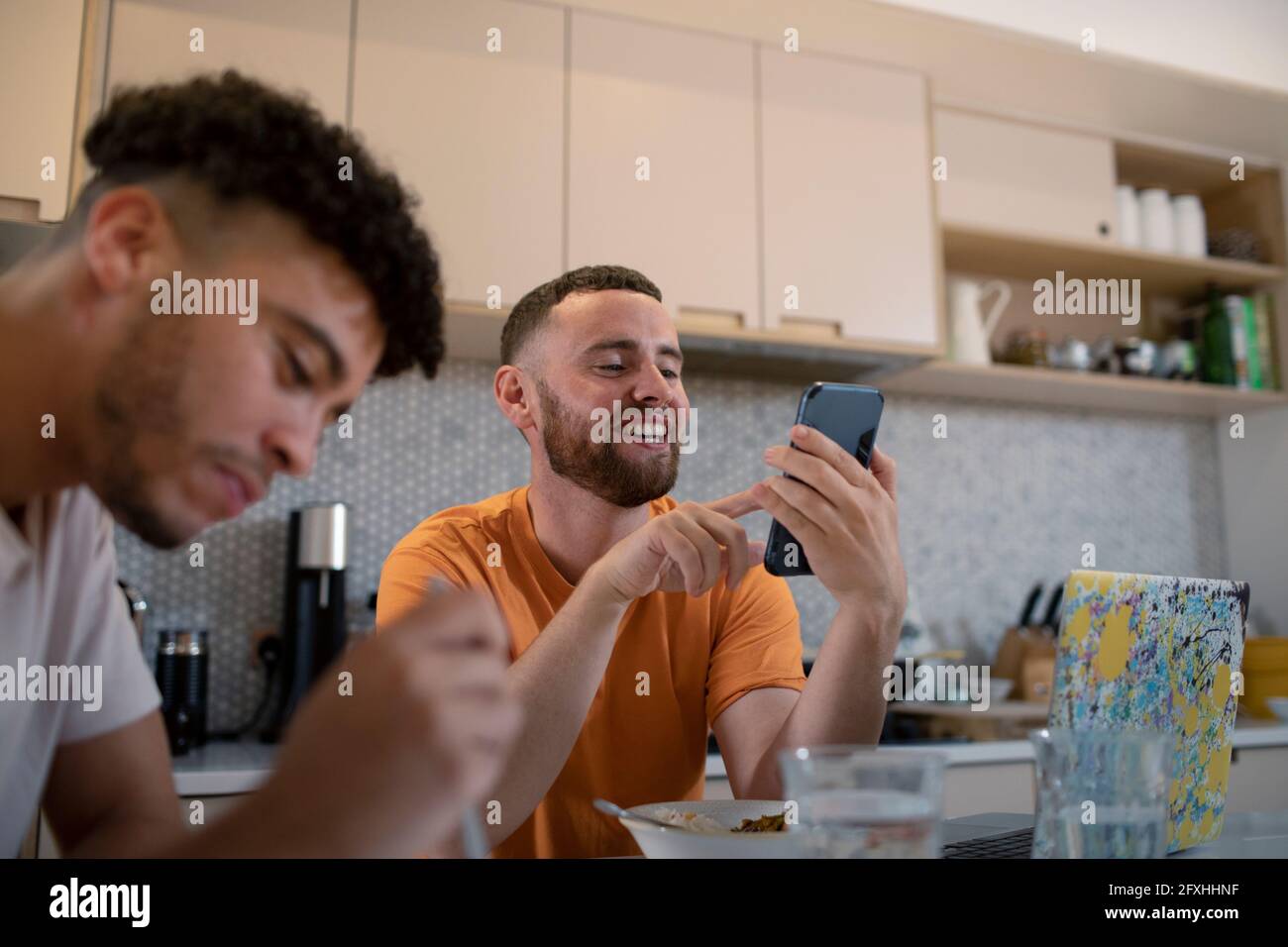 Glücklich Gay männliche Paar mit Smartphone und Essen in der Küche Stockfoto